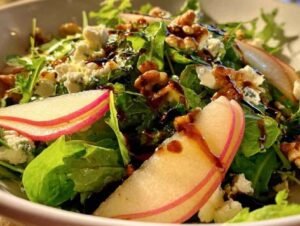 Mesclun de jeunes pousses avec des tranches de poire, du fromage de chèvre émietté et des noix, prêt à être servi.