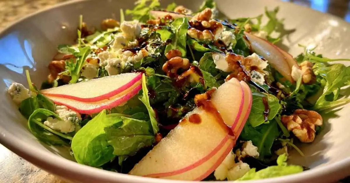 Mesclun de jeunes pousses avec des tranches de poire, du fromage de chèvre émietté et des noix, prêt à être servi.