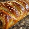Feuilleté roulé à la viande hachée cru, badigeonné de jaune d'œuf et parsemé de sésame, prêt à être cuit.