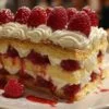 Ingrédients pour la recette du framboisier léger disposés sur un plan de travail en bois : œufs, farine, sucre, framboises et fromage blanc.