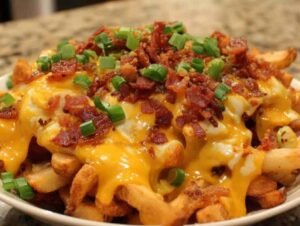 Des frites au four dorées et croustillantes, généreusement recouvertes de cheddar fondu et de morceaux de bacon grillé, parsemées d'oignons verts ciselés.