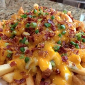 Frites au Cheddar et Bacon 3 Frites dorées sur une plaque de cuisson, en train d'être garnies de cheddar râpé et de lardons avant de retourner au four.