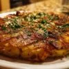 Ingrédients pour la galette de pommes de terre Morteau : pommes de terre râpées, saucisse en dés, tome râpée, oignons hachés et œufs dans des bols séparés sur un plan de travail en bois.