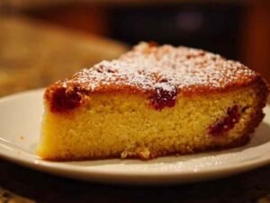 Gâteau breton aux framboises entier, saupoudré de sucre glace et présenté sur un plat de service blanc.