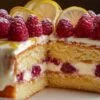 Gâteau citron framboise à deux étages, recouvert d'un glaçage blanc au fromage frais et décoré de framboises fraîches et de rondelles de citron.
