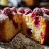 Gâteau fondant aux framboises entier, joliment doré et saupoudré de sucre glace, refroidissant sur une grille de pâtisserie.