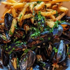 Moules Frites Facile 3 Gros plan sur des moules s'ouvrant dans une grande casserole avec de l'ail, de l'oignon et du persil.