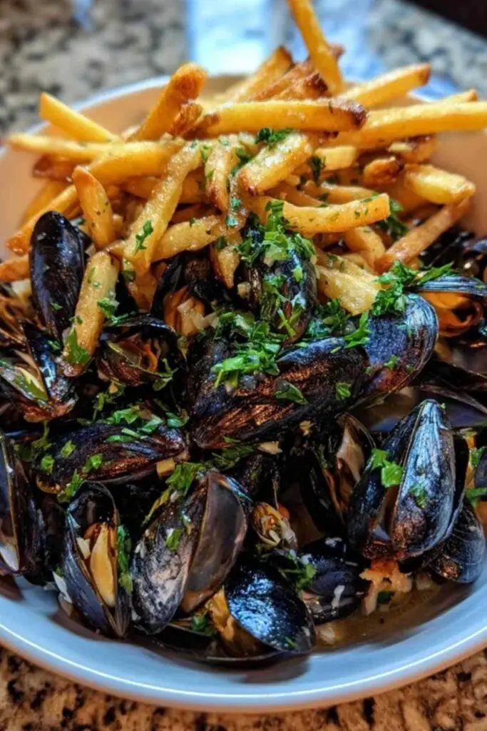 Moules Frites Facile 2 Gros plan sur des moules s'ouvrant dans une grande casserole avec de l'ail, de l'oignon et du persil.