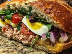 Un pan bagnat maison coupé en deux, révélant ses couches colorées de thon, tomate, œuf et roquette.