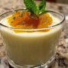 Verrine de panna cotta mascarpone surmontée d'une compotée d'abricot, avec une cuillère à dessert à côté.