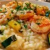 Plat de risotto crémeux aux crevettes et courgettes dans une assiette blanche, garni de persil.