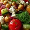Salade de pois chiches, feta, tomates cerises et concombre dans un grand saladier blanc, garnie de menthe fraîche.