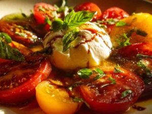 Salade de tomates anciennes colorées et burrata crémeuse dressée sur un plat de service blanc, arrosée de vinaigrette balsamique.