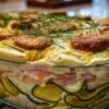 Verrine de tiramisu salé à la courgette et au saumon fumé, décorée d'aneth frais, posée sur une table estivale.