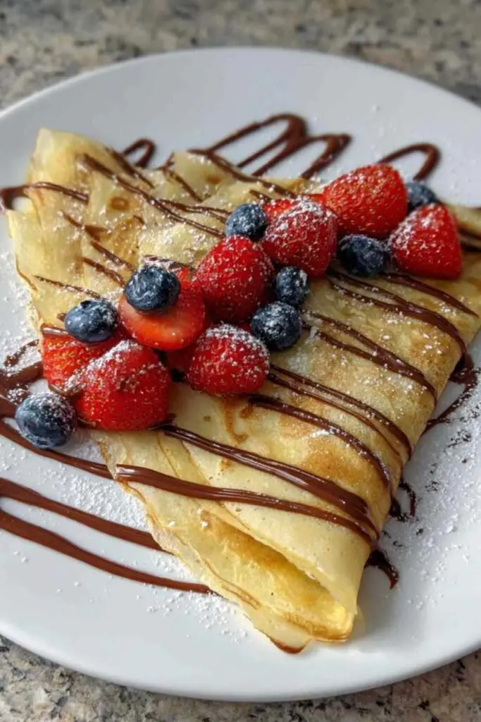 Pile de crêpes dorées garnies de Nutella et fruits frais