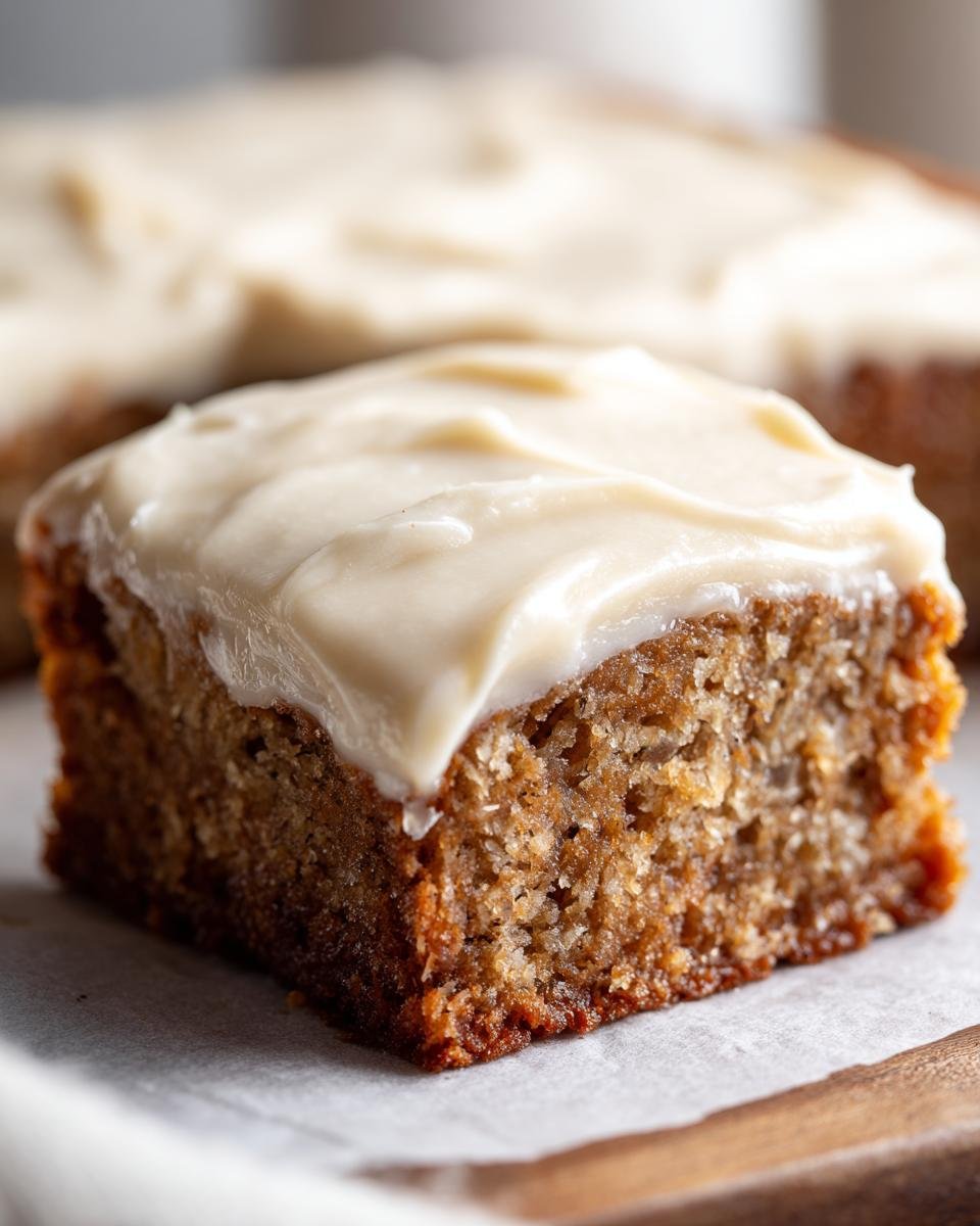 Barres à la banane: 1 recette divinement simple 1 Gros plan d'une barre à la banane moelleuse recouverte d'un glaçage blanc crémeux.