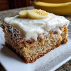Une part de barres à la banane avec un glaçage crémeux et des rondelles de banane sur le dessus.