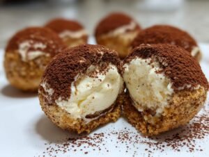 Gros plan sur des boules de tiramisu garnies de cacao en poudre, une est coupée en deux.