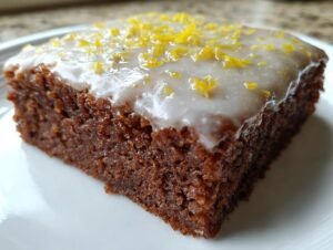 Gros plan d'une tranche de brownies au citron avec glaçage blanc et zestes de citron.