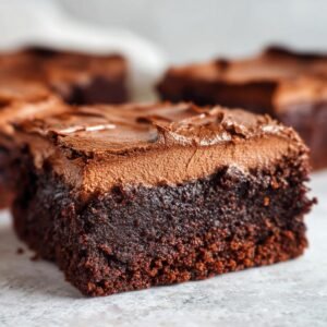 Gros plan sur une tranche de Brownies Mousse Chocolat, avec un glaçage au chocolat onctueux.