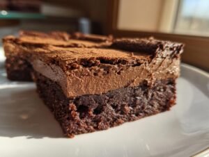 Gros plan sur une tranche de Brownies Mousse Chocolat, avec une base dense et une couche aérienne de mousse au chocolat, saupoudrée de cacao.