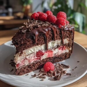 Gros plan d'une part de gâteau au chocolat et framboises, garnie de framboises fraîches et copeaux de chocolat.