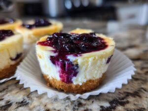 Gros plan sur un mini cheesecake citron myrtille garni de myrtilles et posé dans une caissette en papier.