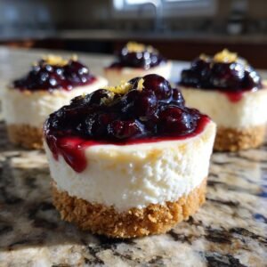 Gros plan sur des mini cheesecakes aux myrtilles et au citron, garniture au coulis de myrtilles et zeste de citron.