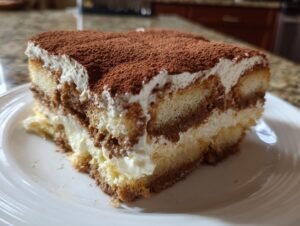 Gros plan d'une part de Tiramisu au Fromage Cottage, avec des couches de biscuits, de crème et de cacao.