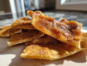 Gros plan de morceaux de toffee aux crackers churros, saupoudrés de cannelle et de sucre, avec un glaçage brillant.