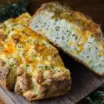 Gros plan d'une tranche de Pain Soda au Cheddar et Herbes, avec du fromage fondu et des herbes visibles dans la mie aérée.