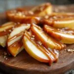 Gros plan de tranches de pommes au caramel, arrosées de sauce caramel et saupoudrées de miettes.