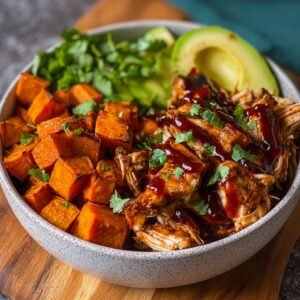 Gros plan d'un bol de poulet BBQ effiloché, patates douces rôties, avocat et coriandre fraîche.