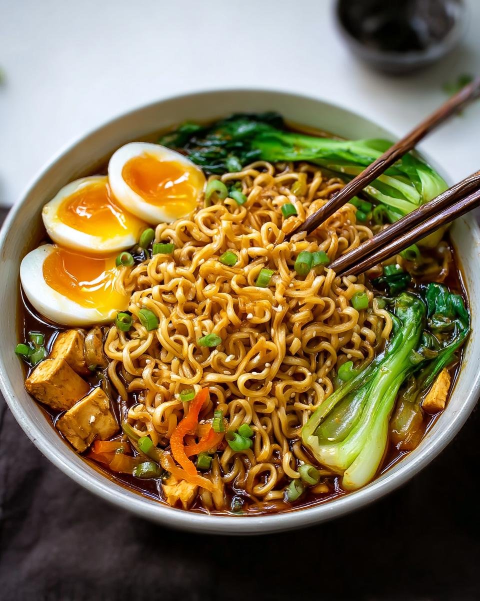 Bol de nouilles ramen protéinées faciles avec œufs mollets, tofu, légumes verts et oignons verts.