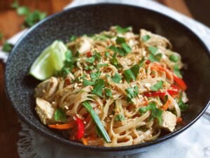 Healthy Pad Thai : 400 Calories, 35g Protéines Plat de Pad Thaï au poulet sain avec nouilles de riz, légumes colorés et garniture d'herbes fraîches.